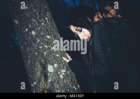 Ragazza di tenere su un albero nella foresta di notte Foto Stock