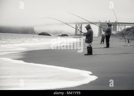 Una foto in bianco e nero di persone di pesca su una spiaggia di fronte al Golden Gate Bridge su un nebbioso giorno Foto Stock