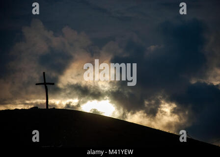 Una semplice croce di legno in cima ad una collina stagliano contro il cielo luminoso al tramonto Foto Stock