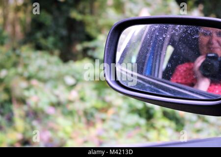 Immagine Di Donna sorridente tenendo selfie con la fotocamera in riflessione di macchina sporca specchietto laterale Foto Stock