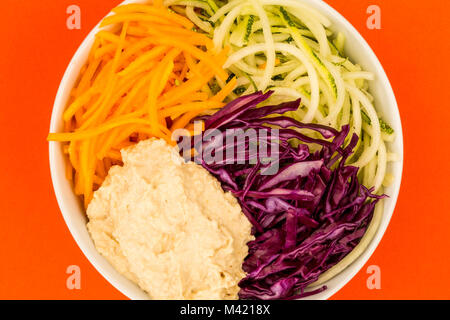 Vegan o vegetariano insalatiera con cavolo rosso Zucchine carote e Hummus contro uno sfondo rosso Foto Stock