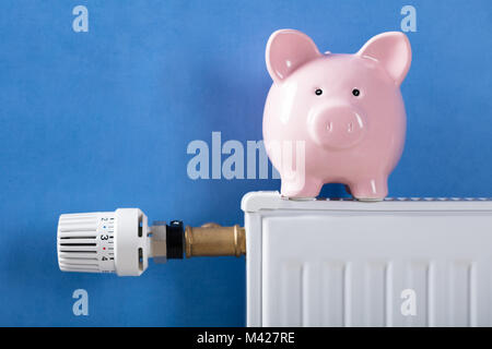 Close-up di salvadanaio sul radiatore di riscaldamento contro sfondo blu Foto Stock