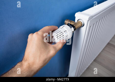 Persona della mano la regolazione della temperatura sul termostato per il controllo del calore nel sistema di riscaldamento centrale Foto Stock