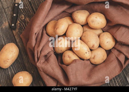 Le patate in una sacca di tela con la lama di un coltello per pulire le verdure sul fondo naturale Foto Stock