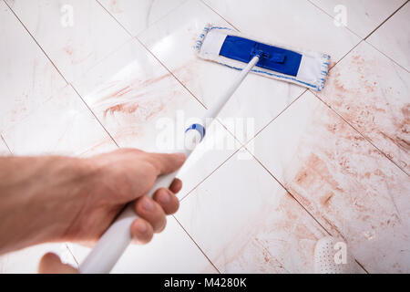 Elevato angolo di visione della persona che tiene il mop e con straccio sporchi il pavimento della cucina a casa Foto Stock