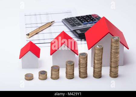 Pila di monete nella parte anteriore del modello di casa e documenti su sfondo bianco Foto Stock