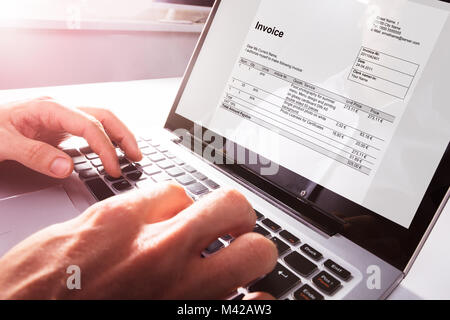 Close-up di imprenditore il mani lavorando su fattura su computer portatile in ufficio Foto Stock