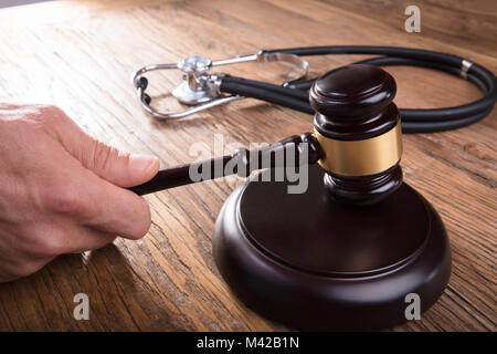 Close-up di un giudice mano martello colpisce con uno stetoscopio sulla scrivania di legno nelle aule di tribunale Foto Stock