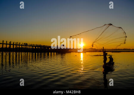 Un pescatore su una barca è di gettare la sua rete nel lago Taungthaman accanto a U Bein Bridge a sunrise Foto Stock