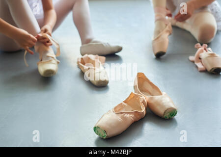 Ballet pointe scarpe, sfondo sfocato. Ballerina mettendo sul ballet pantofole seduto sul pavimento. Calzature per ballerini. Foto Stock