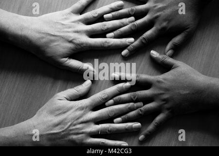Guardando verso il basso su quattro cinquanta anni di mani femminili sparsi, che giace piatto su una tabella, le due mani sulla sinistra una asiatica di mani e due sulla destra un Foto Stock
