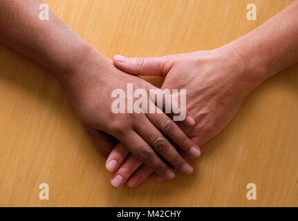 Vista aerea di due cinquanta anni di mani femminili e bracci inferiori posti sullaparte superiore di ogni altra la mano superiore è asiatico e la mano di fondo è caucasico, t Foto Stock