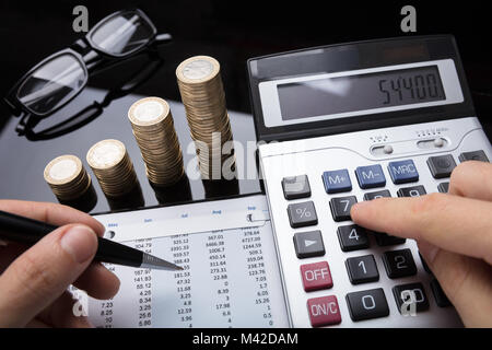 Close-up di un imprenditore la mano il calcolo dei dati finanziari con monete impilate su scrivania Foto Stock