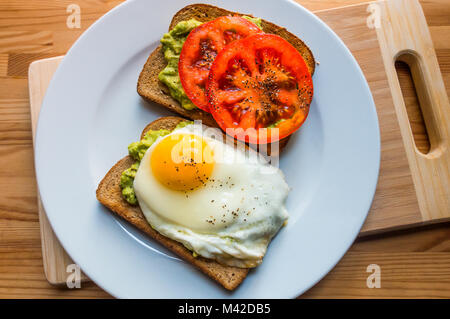 Avocado toast con fette di pomodoro e un uovo fritto Foto Stock