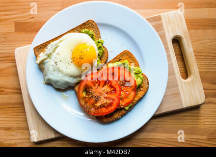 Avocado toast con fette di pomodoro e un uovo fritto Foto Stock