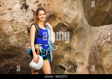 Ritratto della bella ragazza che sta ai piedi della montagna con rock arrampicata attrezzature Foto Stock