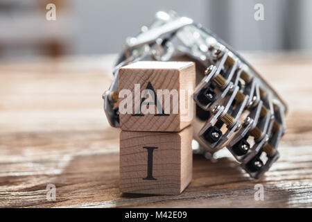 Il Robot la mano che trattiene i blocchi di legno con una e ho Alfabeto sulla scrivania in legno Foto Stock