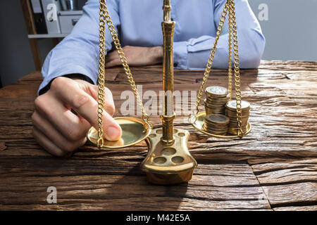 Close-up di un imprenditore di bilanciamento delle monete impilate sulla giustizia scala con il suo dito Foto Stock