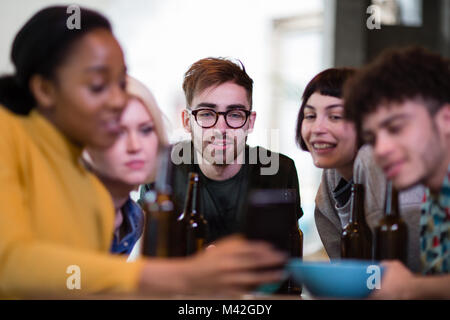 Gruppo di amici alla ricerca di uno smartphone insieme in un pub Foto Stock