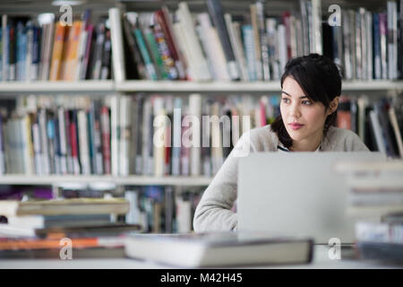 Studente utilizzando laptop in biblioteca Foto Stock