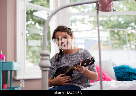 Ragazza che gioca un ukulele guardando la fotocamera Foto Stock