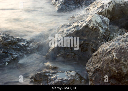 Le rocce che emergono dal mare sono illuminate dal sole al tramonto. Foto Stock