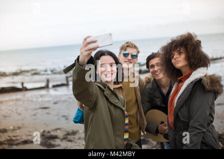 Un gruppo di giovani amici adulti prendendo un selfie su una spiaggia in inverno Foto Stock