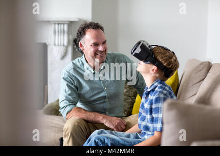 Boy utilizzando un auricolare VR gioco a casa con il Padre Foto Stock