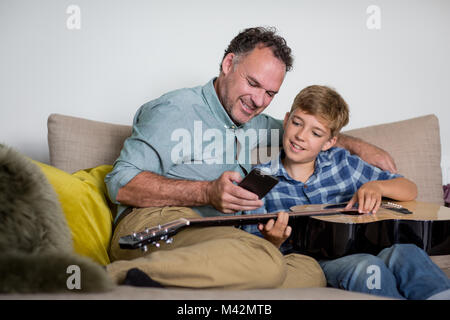 Padre figlio di insegnamento come suonare la chitarra usando uno smartphone Foto Stock