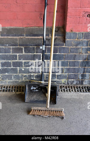 Una paletta e spazzola appoggiata contro il muro su una stazione piattaforma usata per spazzare fino la lettiera e mantenendo le piattaforme ordinate. spazzamento e pulizia. Foto Stock