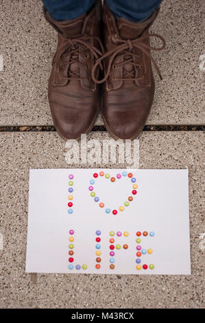 La carta con le parole "I Love Life" sul terreno e la donna con le scarpe marrone vicino ad essa Foto Stock