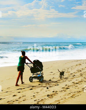 Donna con una carrozzina e un cane a piedi dalla spiaggia. Isola di Bali, Indonesia Foto Stock