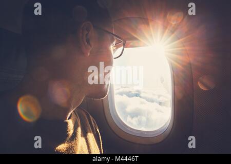 Giovane uomo guardando fuori attraverso la finestra del velivolo durante la bellissima alba. Foto Stock