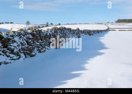 Parete di roccia calcarea getta un' ombra sulla mattina fresca neve. Bradwell, Peak District, Derbyshire, in Inghilterra. Foto Stock