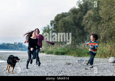 Ragazzo e le giovani donne in esecuzione con il cane lungo il fiume, Calolziocorte, Lombardia, Italia Foto Stock