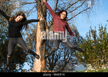Due giovani donne jumping metà aria nel bosco, Calolziocorte, Lombardia, Italia Foto Stock