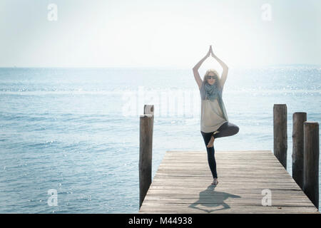 Donna sul molo in equilibrio su una gamba nella posa di yoga Foto Stock