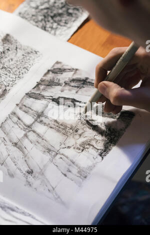 Artista maschile disegno in sketchbook in artists studio, sulla spalla vista Foto Stock