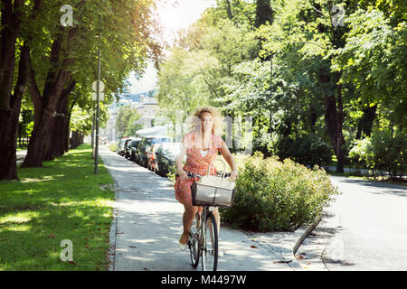 Donna di pedalare sulla bicicletta in strada alberata, Innsbruck, in Tirolo, Austria, Europa Foto Stock