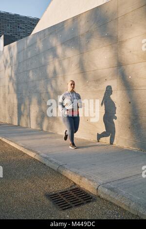 Sinuosa femmina giovane runner che corre lungo il marciapiede Foto Stock