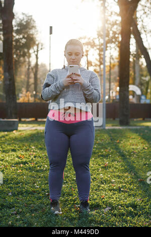 Sinuosa giovane donna formazione nel parco, guardando a smartphone Foto Stock