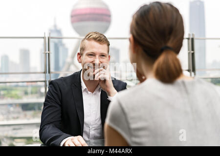 Sulla spalla vista del giovane imprenditore e la donna avente incontro al cafè sul marciapiede in Shanghai centro finanziario di Shanghai, Cina Foto Stock