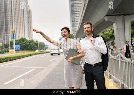 Giovane imprenditrice e uomo salutando un taxi in città, Shanghai, Cina Foto Stock