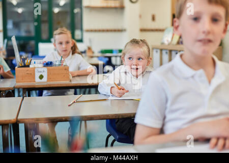 Studentesse primario e ragazzo facendo lavori scolastici a banchi Foto Stock