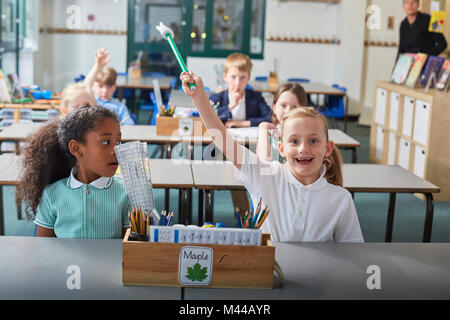 Schoolgirl con la sua mano alzata nella scuola primaria lezione in aula Foto Stock