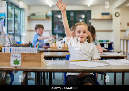 Schoolgirl con la mano sollevata in aula presso la scuola primaria Foto Stock