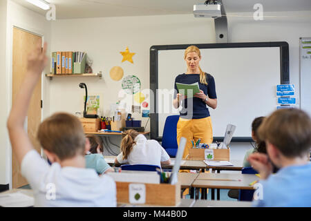 Scolaro con la mano alzata nella lezione in aula presso la scuola primaria Foto Stock