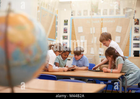 Scolare e ragazzi guardando compresse digitale nella lezione in aula presso la scuola primaria Foto Stock