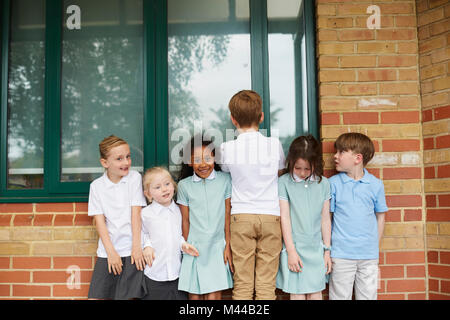 Scolare e ragazzi in piedi in fila al di fuori di edifici scolastici della scuola primaria, ritratto Foto Stock