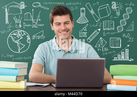 Sorridente studente maschio utilizzando Laptop contro la Lavagna Verde in aula Foto Stock